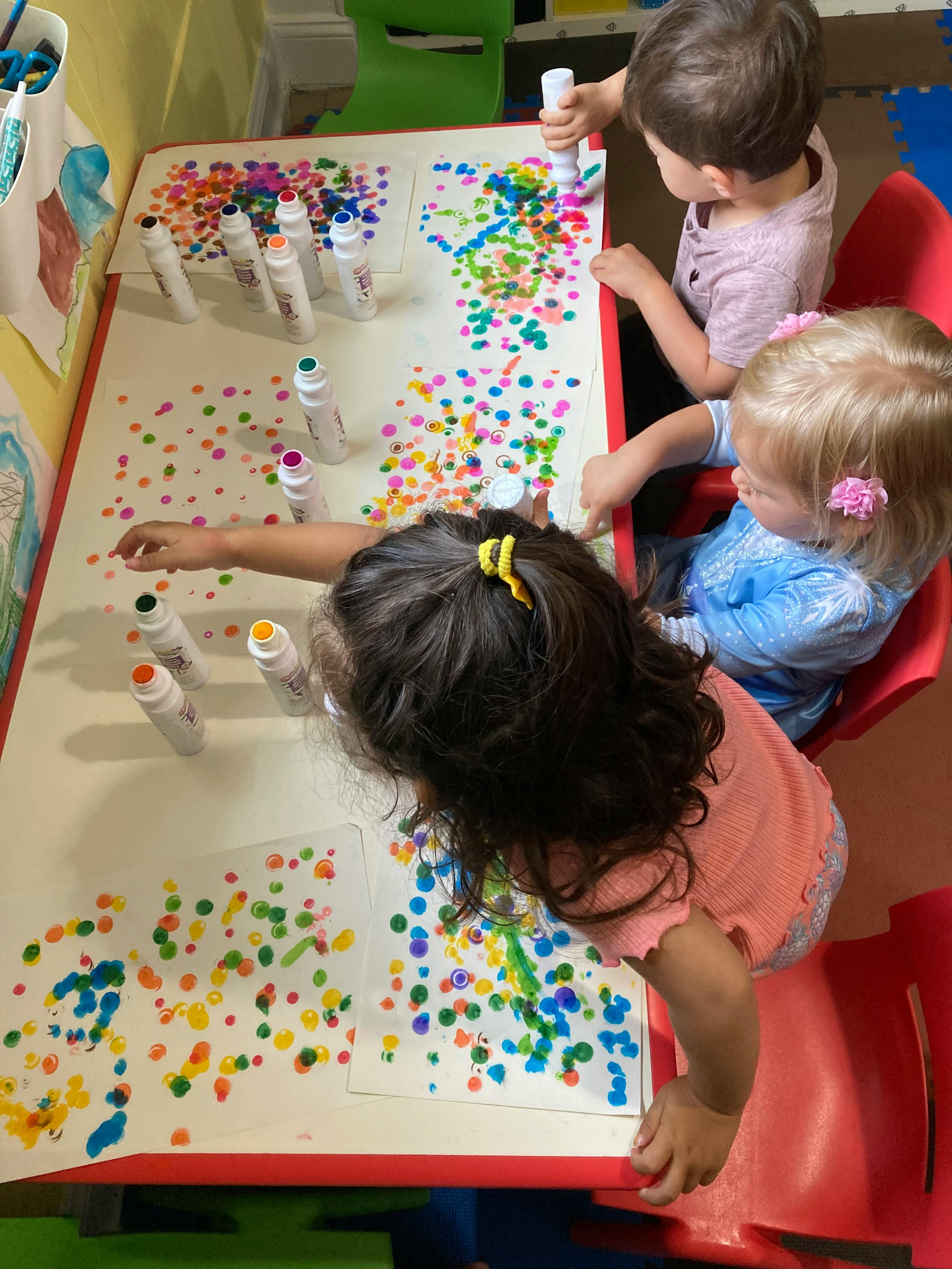 Three children painting with dot markers at a table