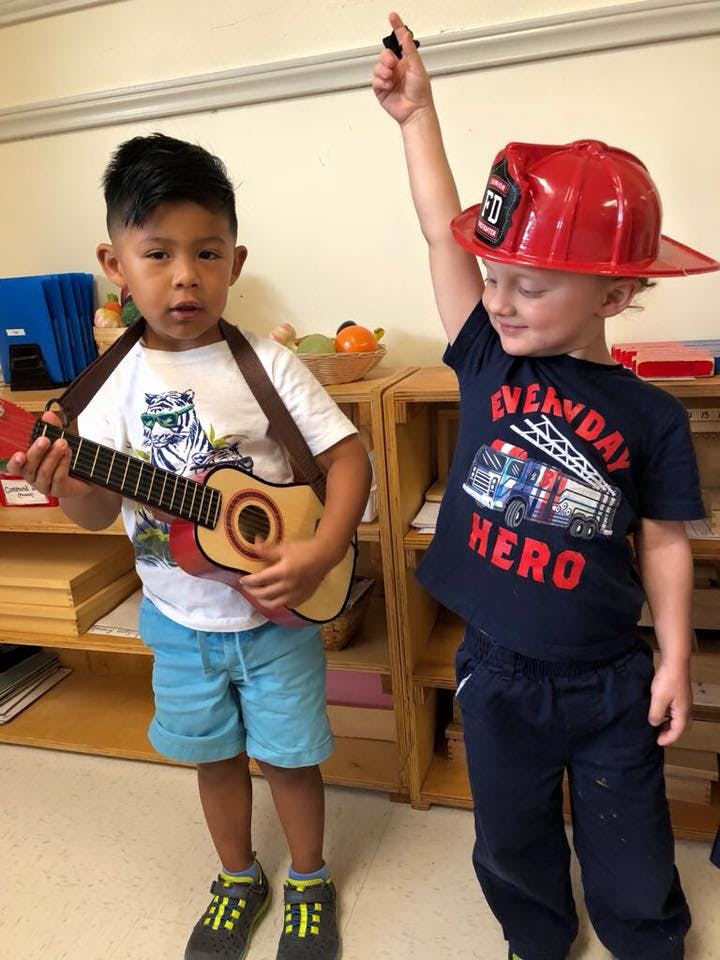 Child playing a toy guitar next to a child in a firefighter hat