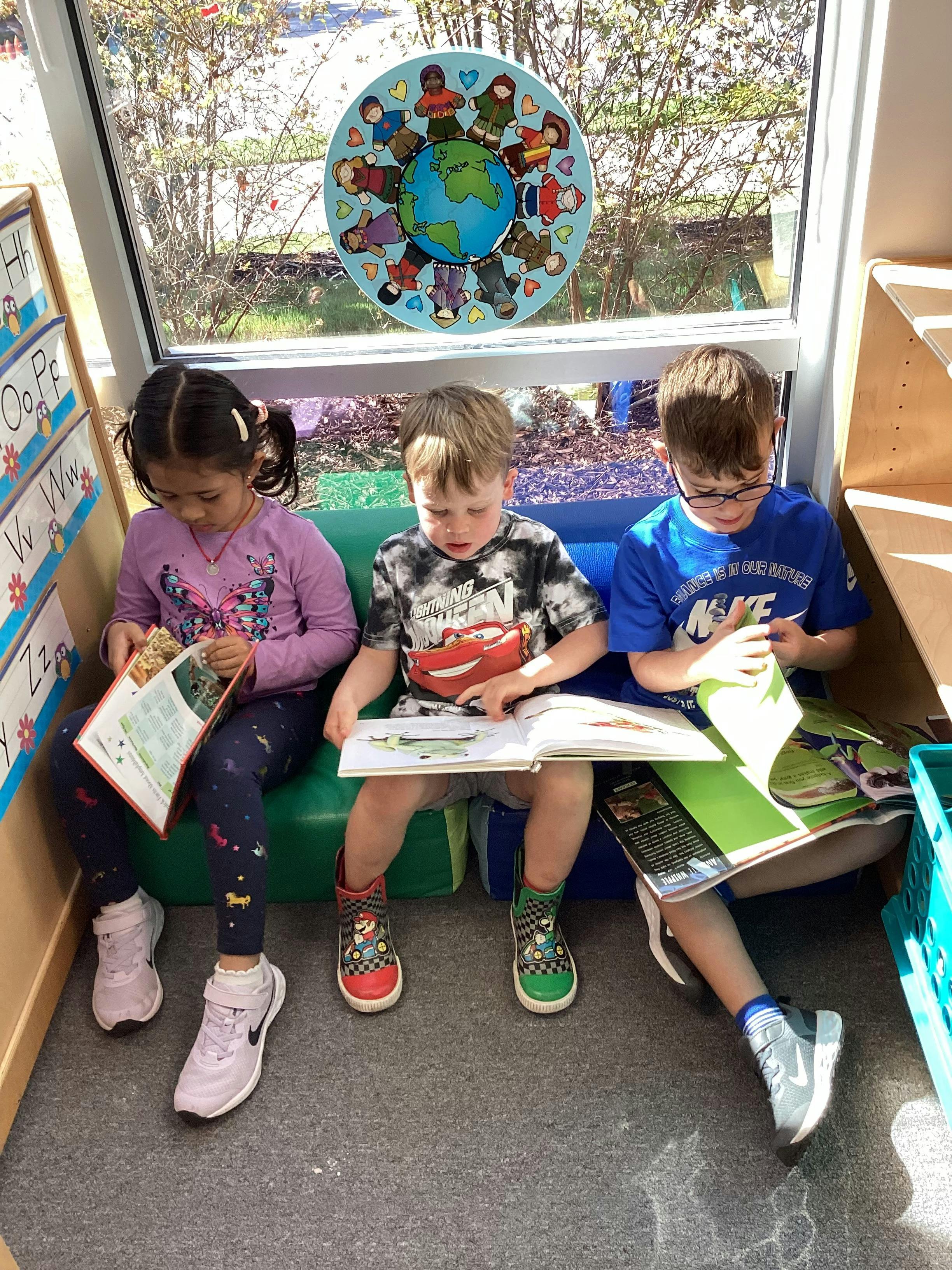 Three children sitting and reading books in a classroom