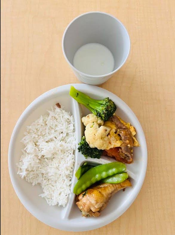 A divided plate with rice, chicken, snow peas, and a broccoli and cauliflower mix