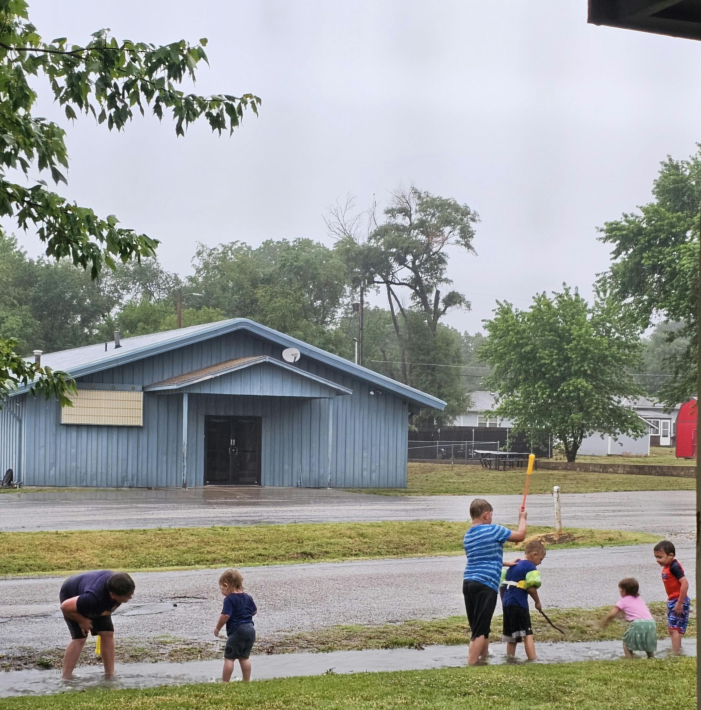 Children playing in puddles on a cloudy day, with a building in the background