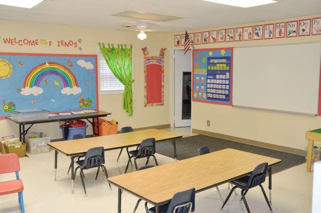 Empty classroom with small tables and chairs, bulletin boards on walls