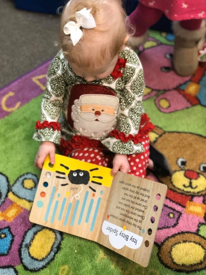 Child in Santa outfit looking at a book with "Itsy Bitsy Spider" text