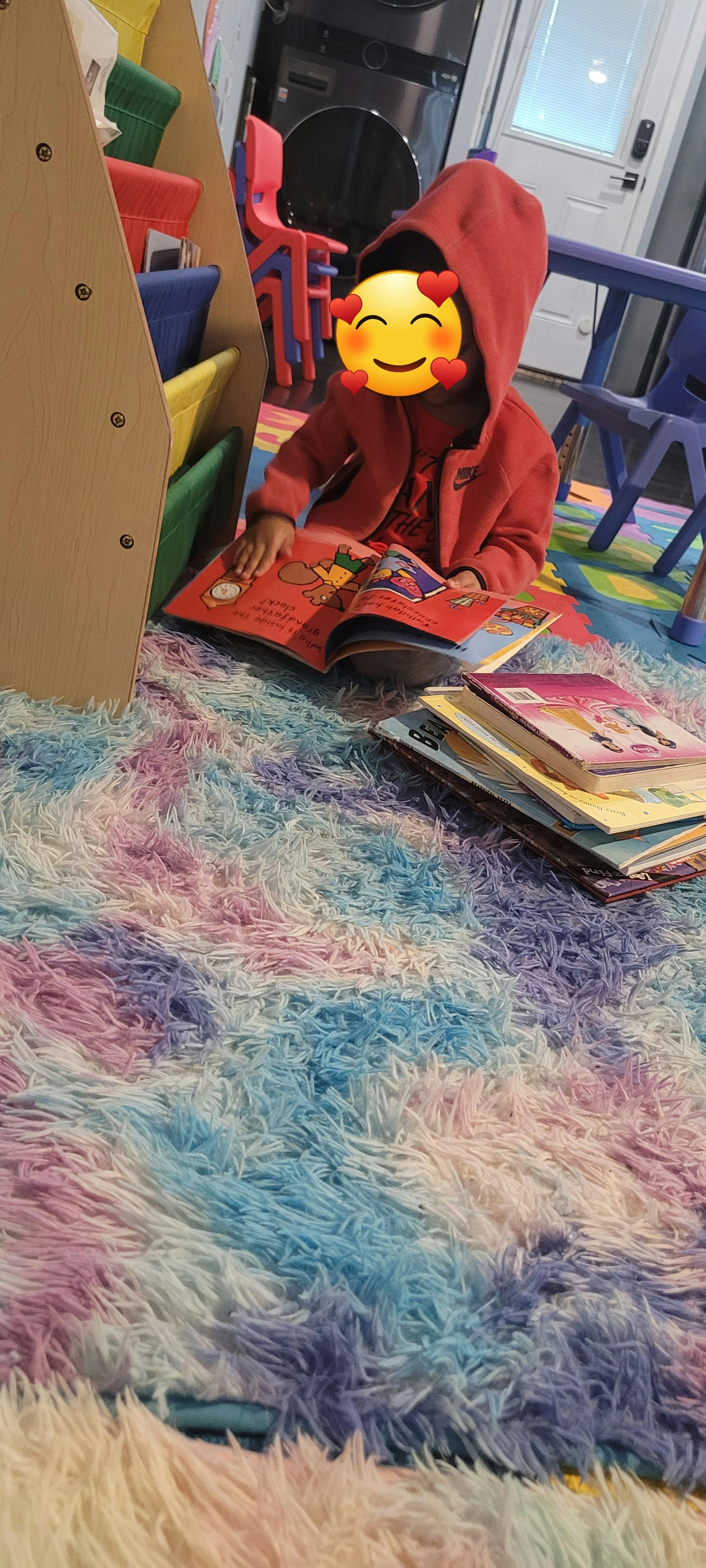 Child in a red hoodie reading a book on a colorful rug
