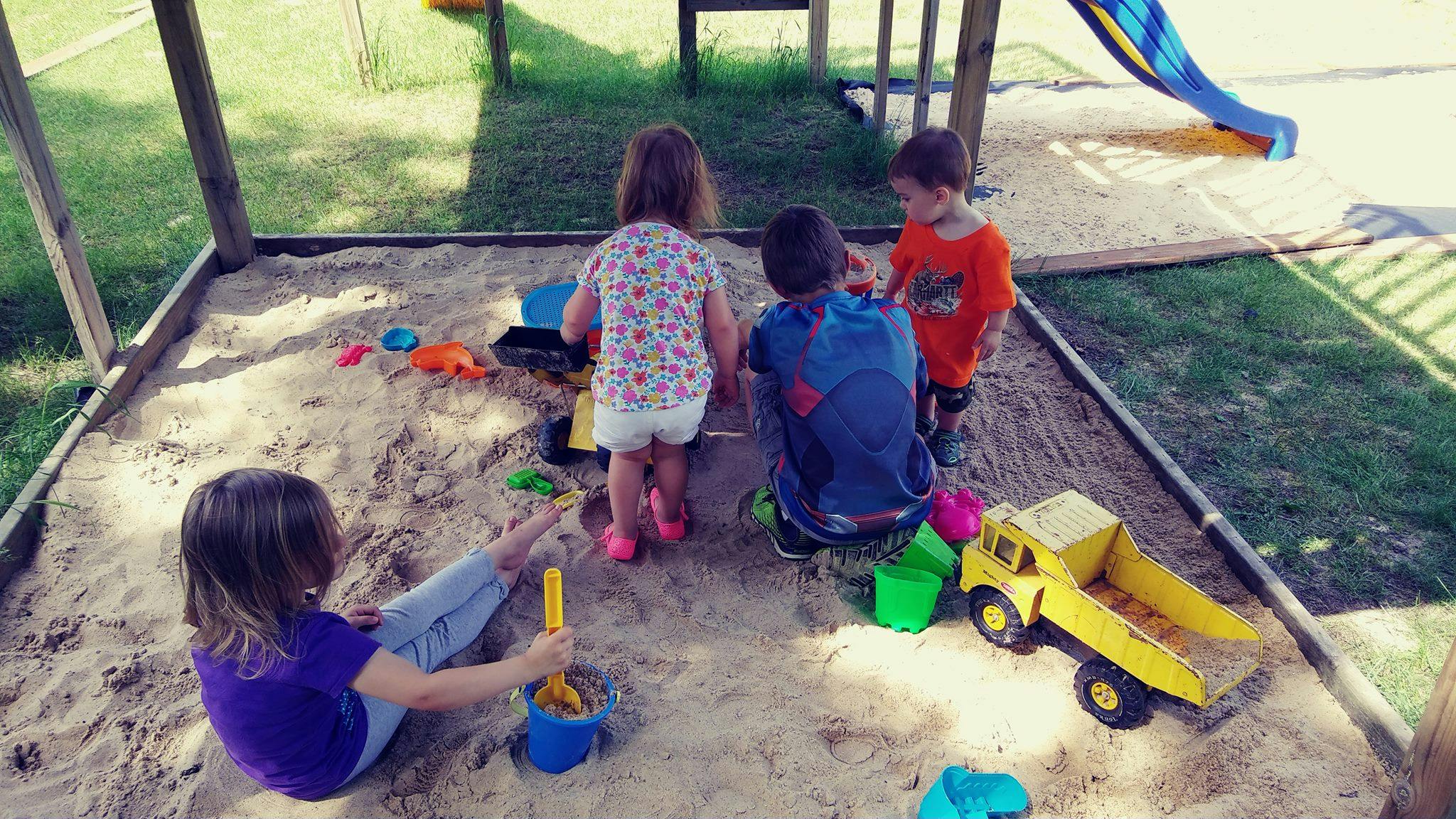 Four children playing in a sandbox with toys