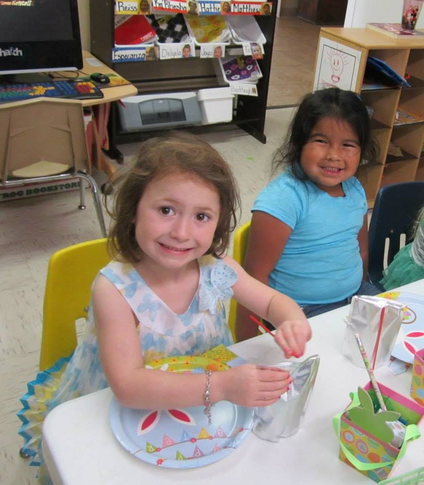 Two children sitting at a table, one holding a craft item