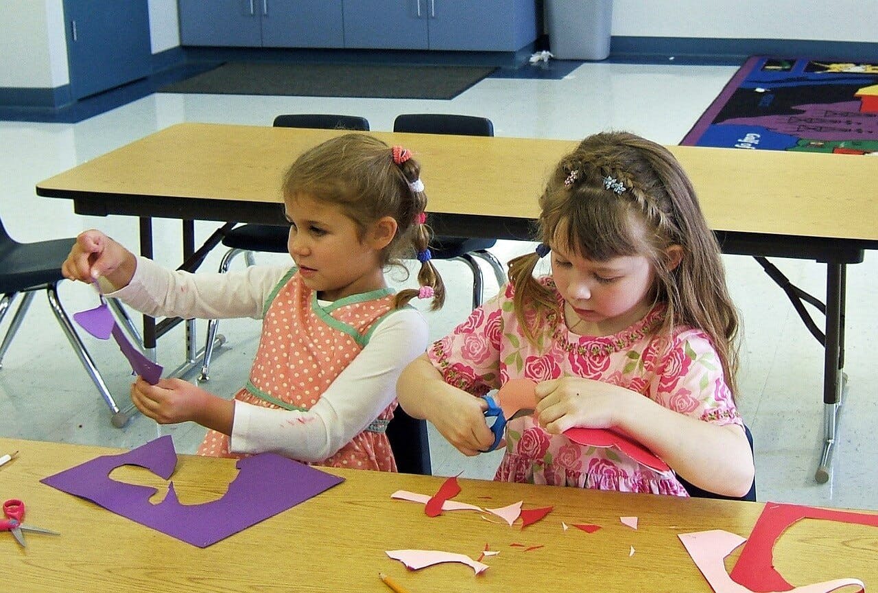 Two children cutting paper shapes at a table