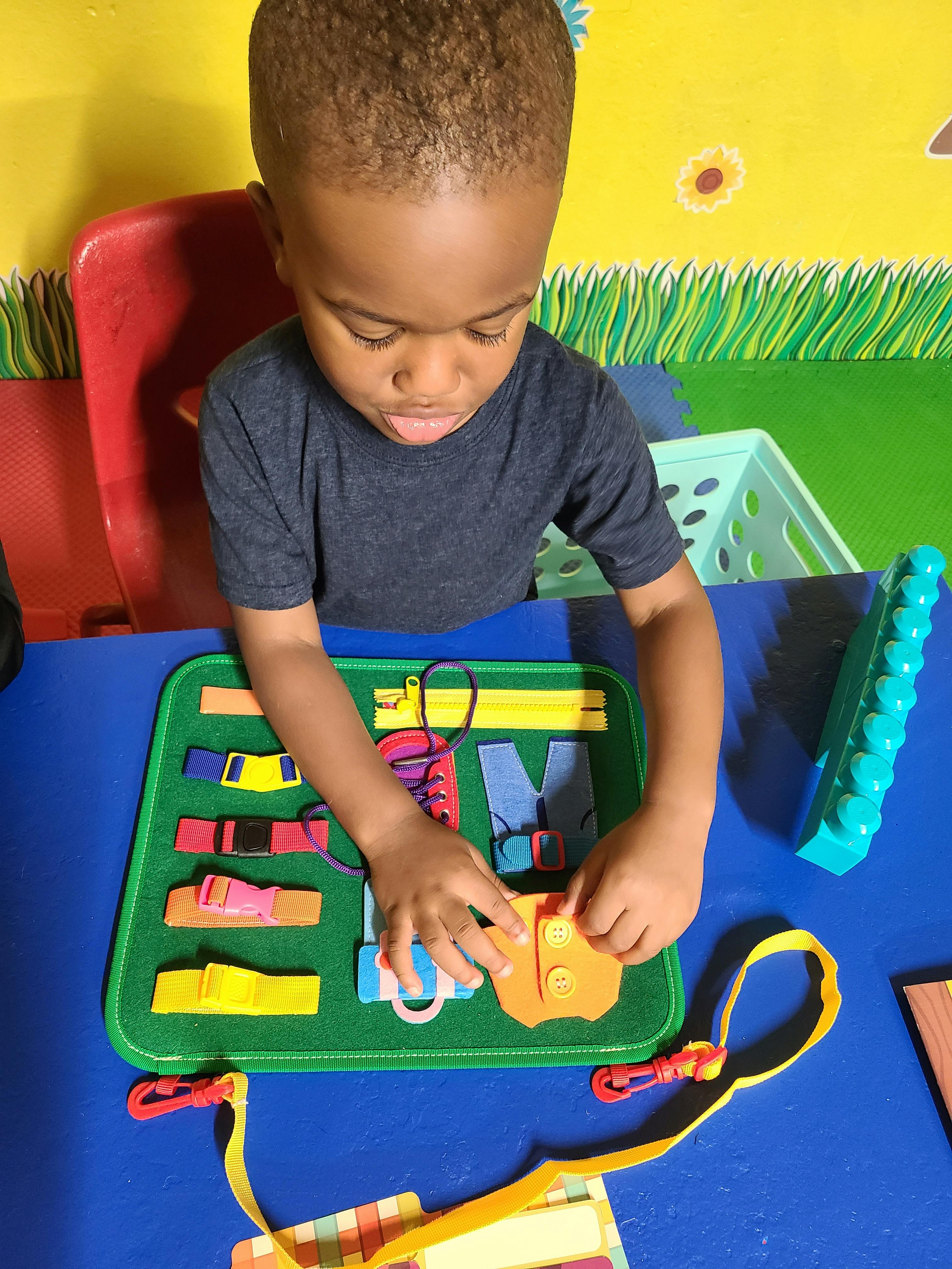 Child playing with a green activity board with various fasteners