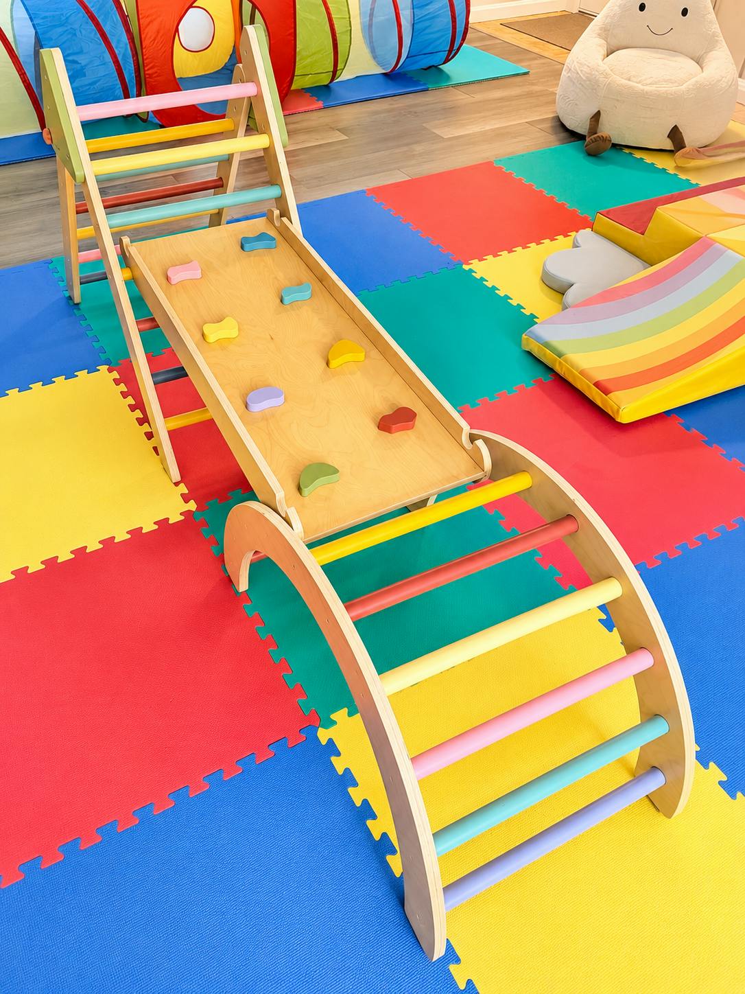 Wooden climbing playset with ramp and colorful rungs on a playroom floor