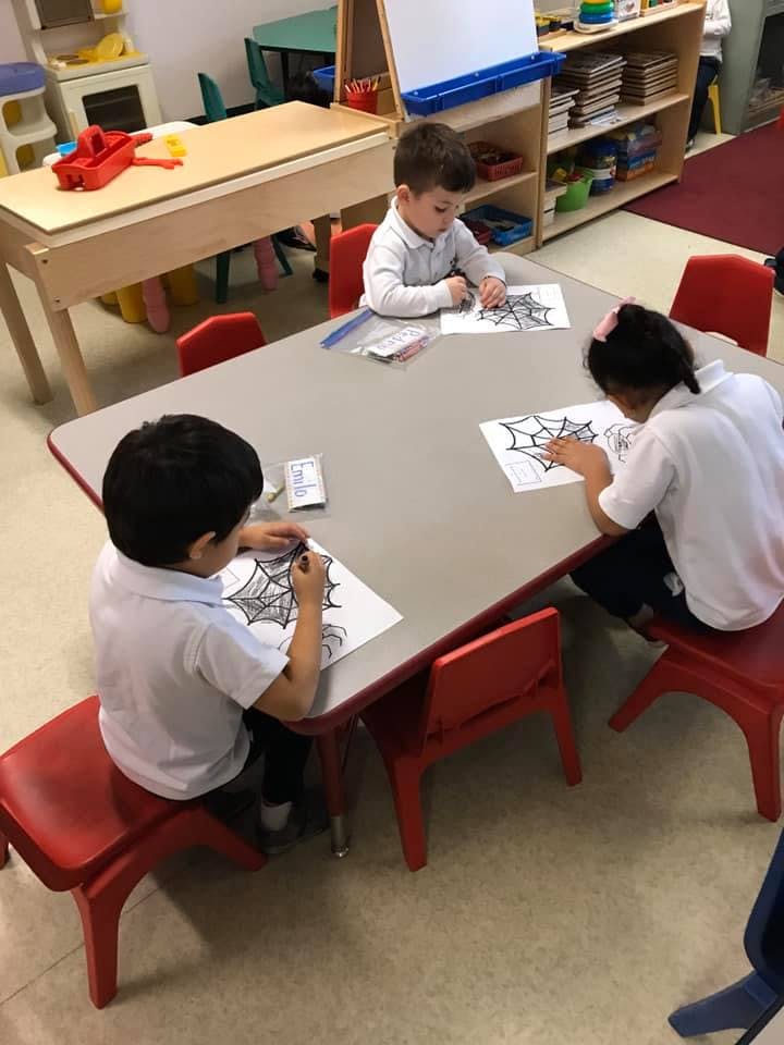 Three children coloring at a table in a classroom