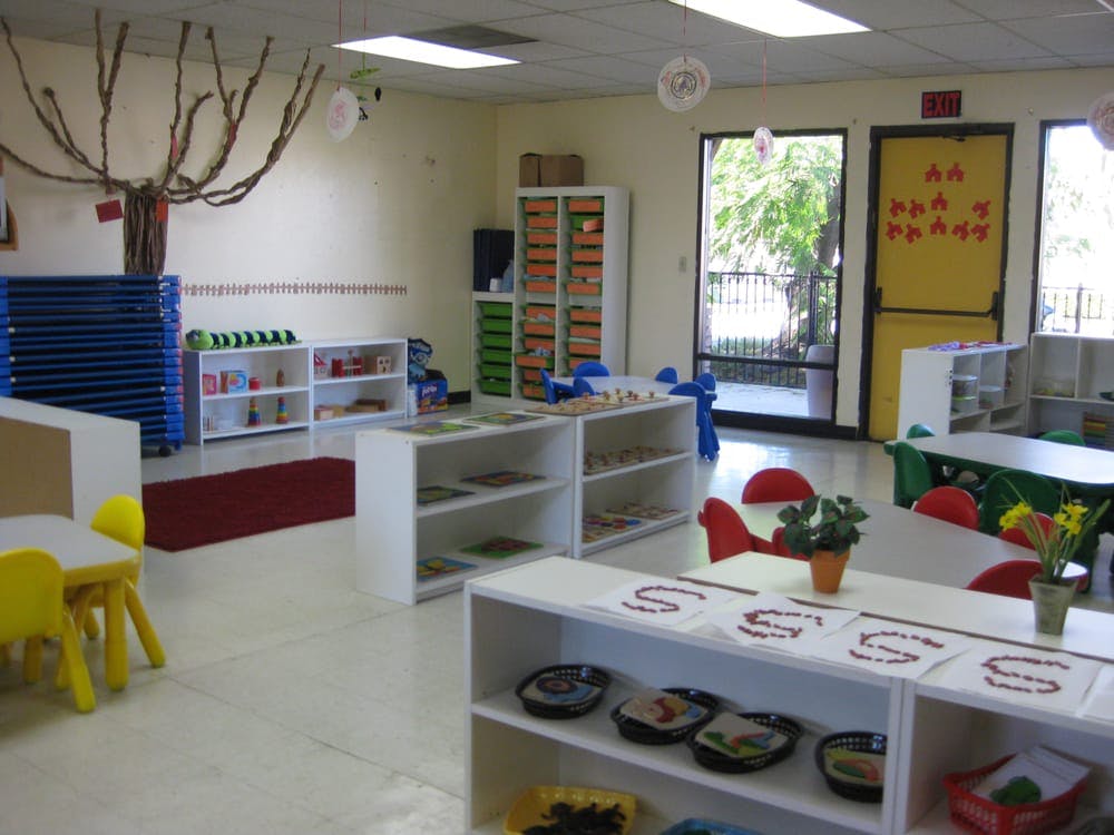 Classroom with small tables and chairs, shelves with learning materials
