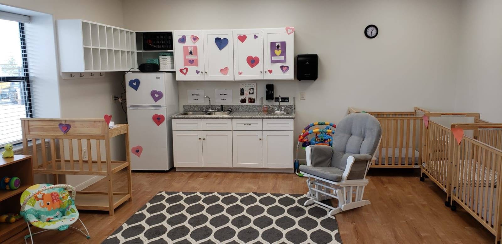 Nursery room with cribs, a rocking chair, and a small kitchen area