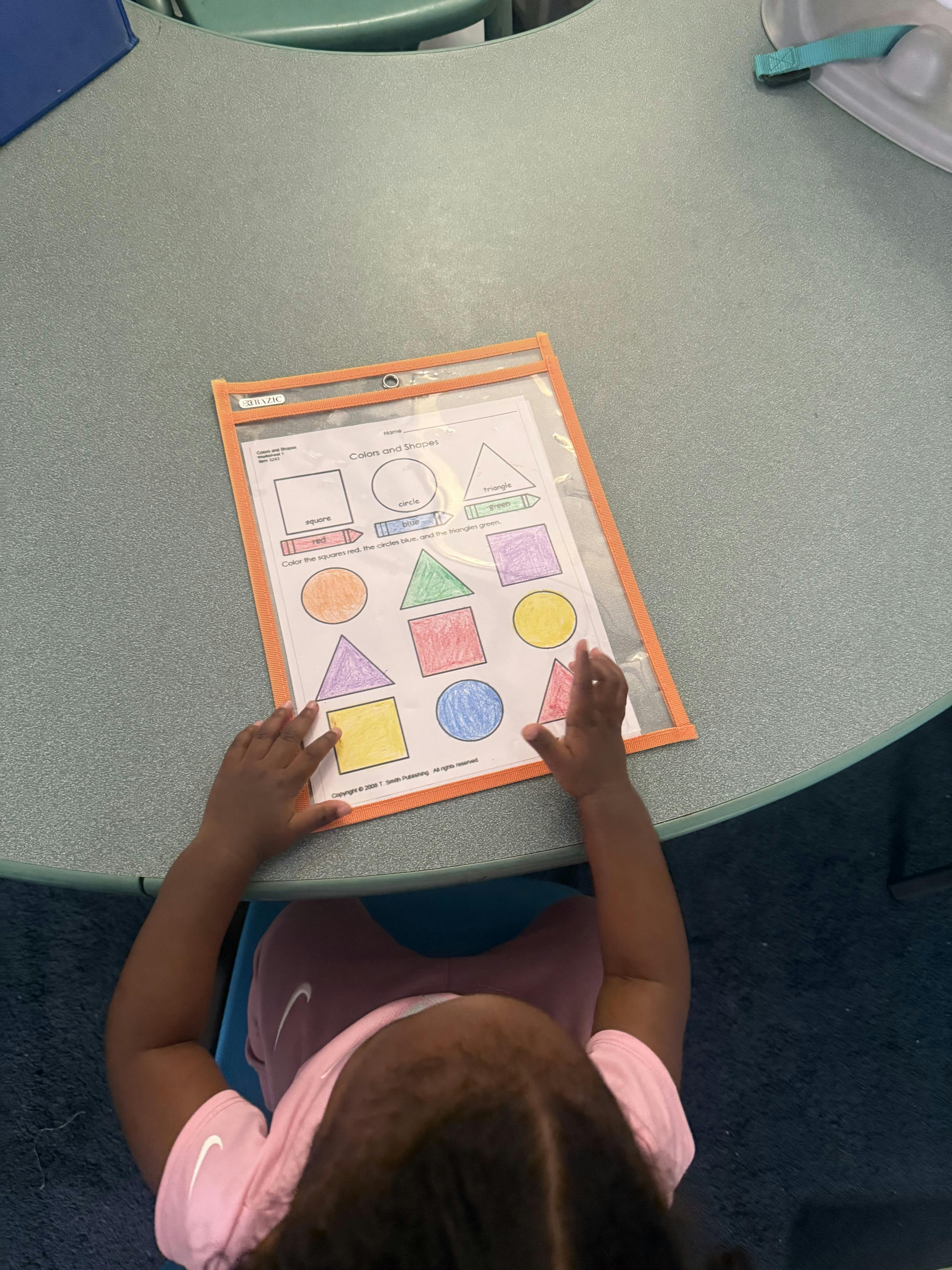 Child working on a colors and shapes worksheet at a table