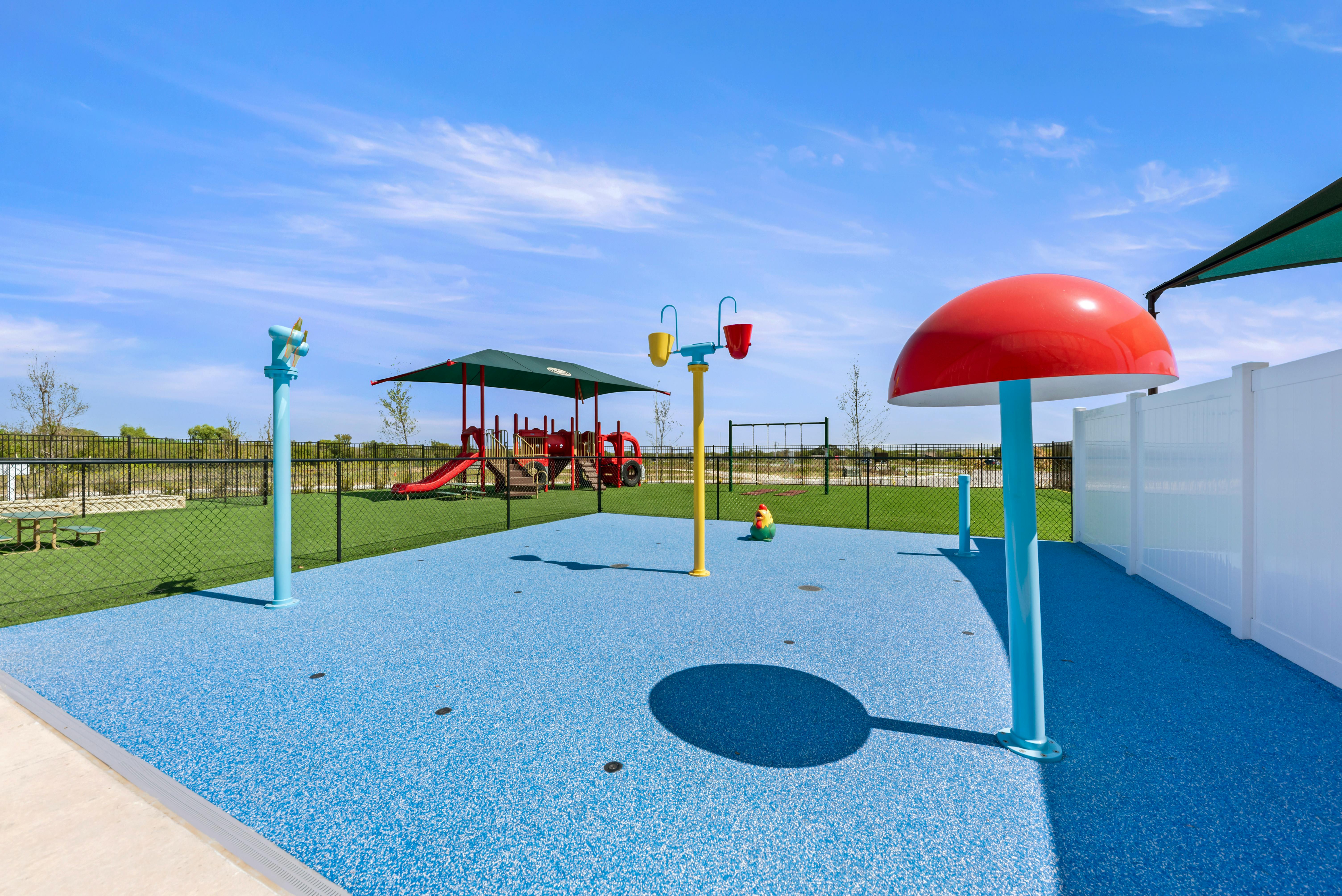 A colorful splash pad with a playground in the background