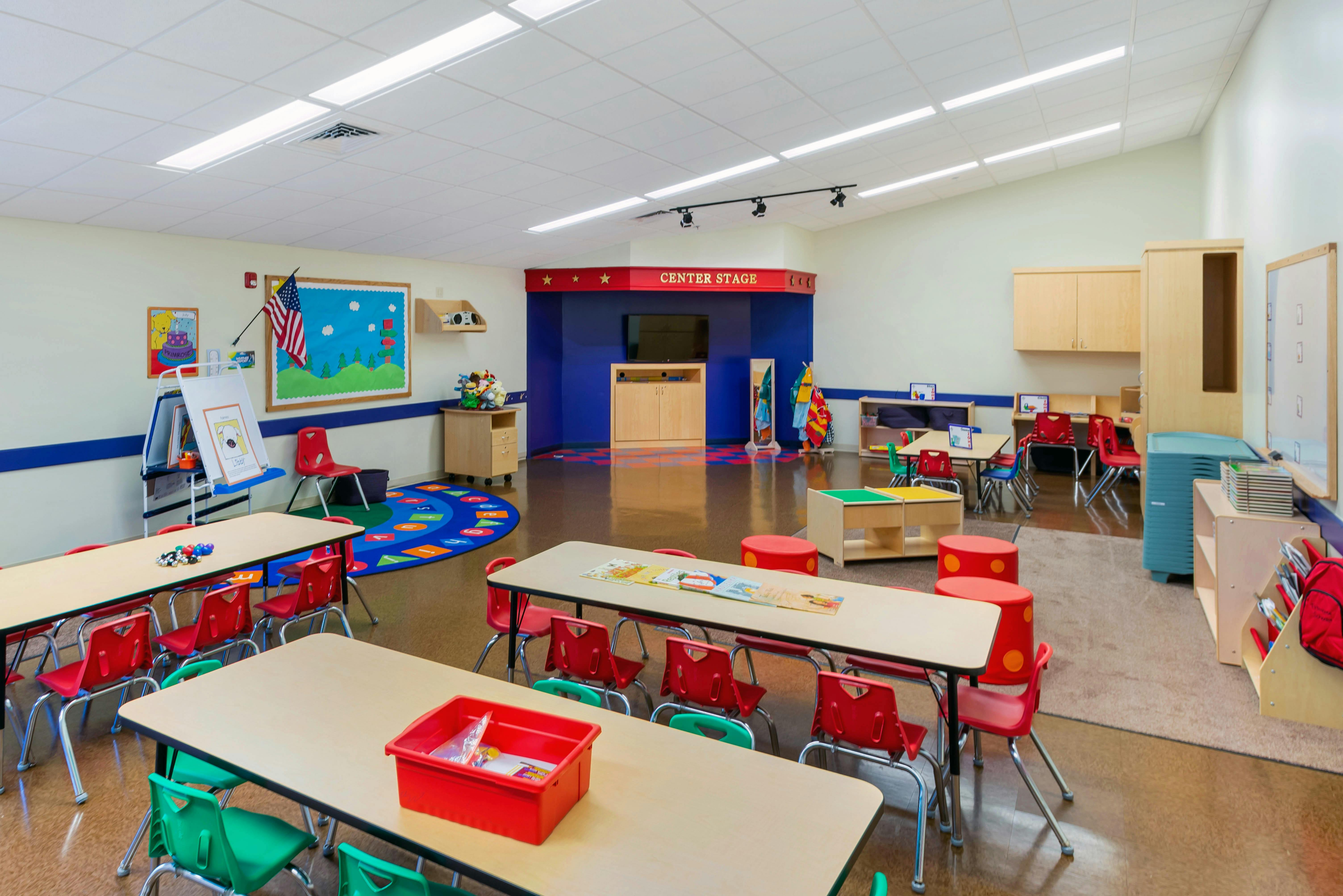 Classroom with child-sized tables and chairs, a play area, and a "CENTER STAGE" sign