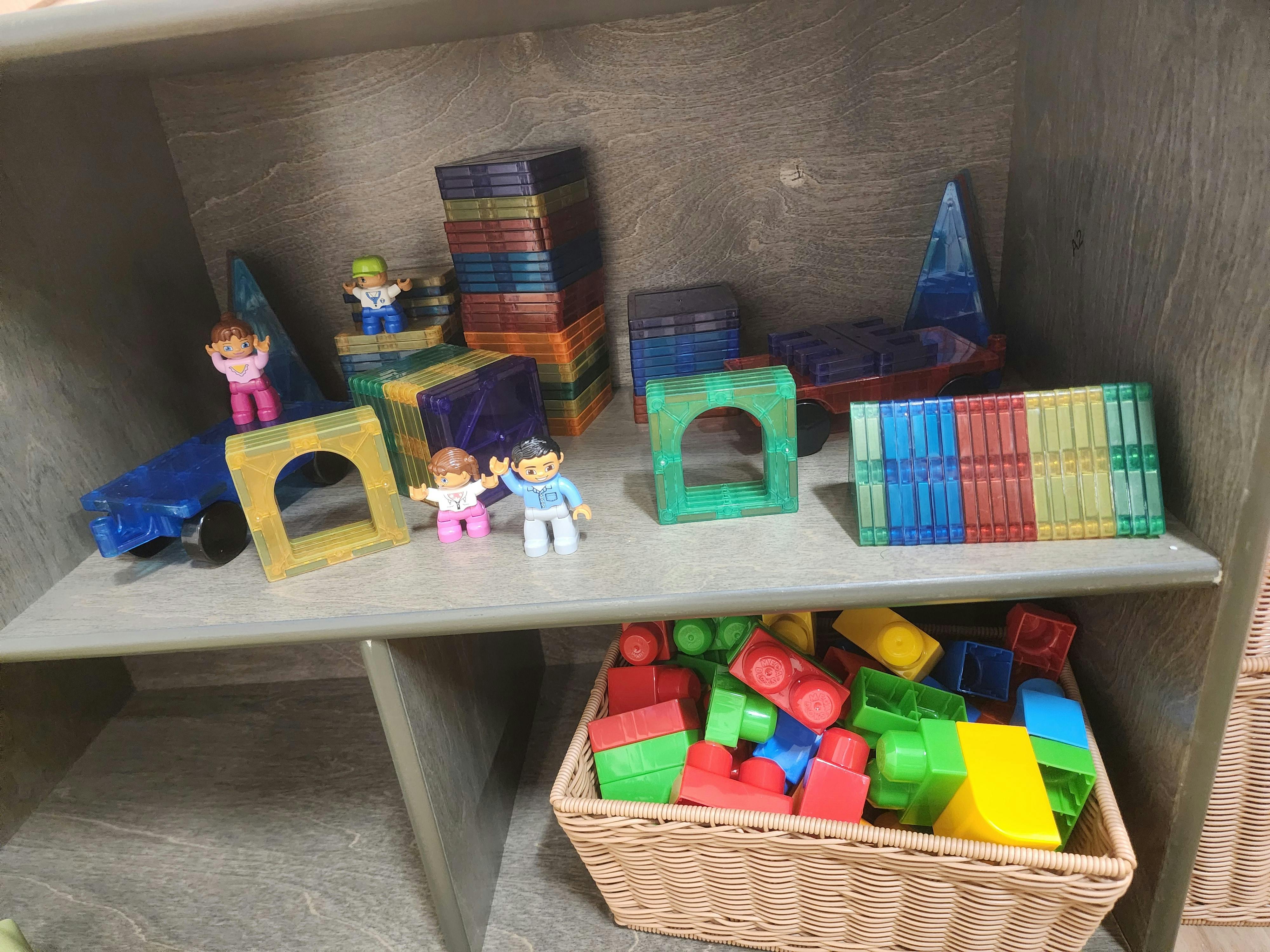 A shelf with plastic magnetic tiles, figurines, and a basket of plastic blocks