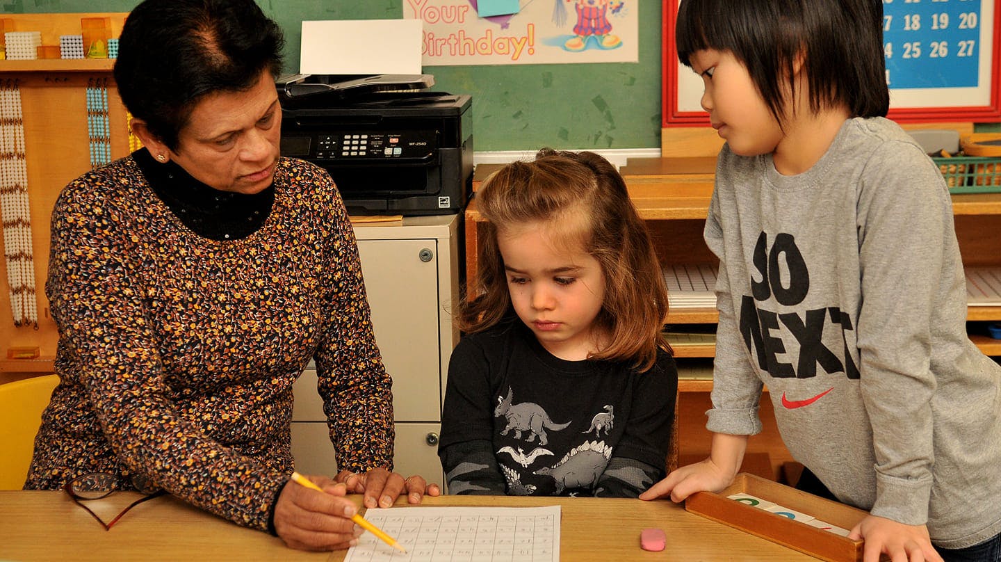 Person helping two children with schoolwork at a desk