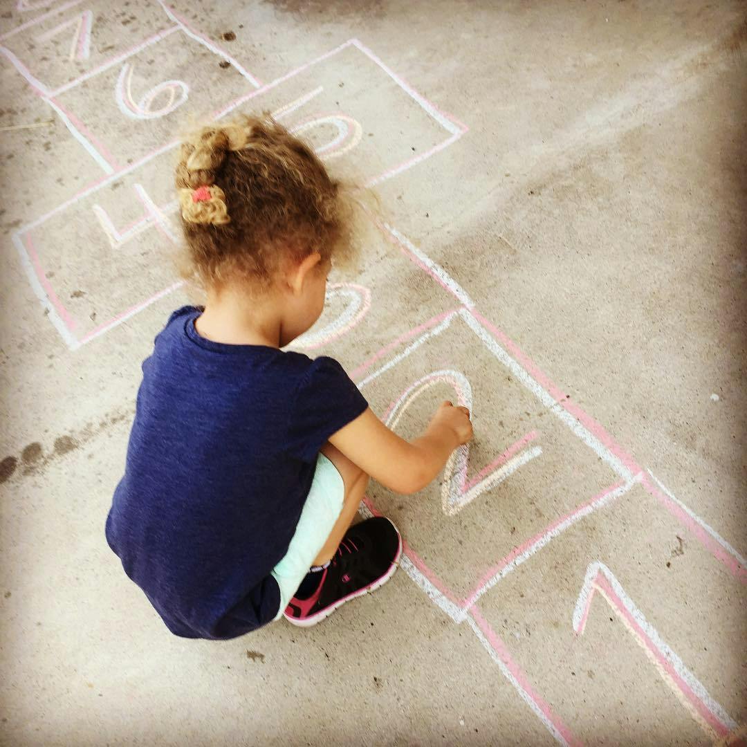 Child drawing hopscotch on pavement