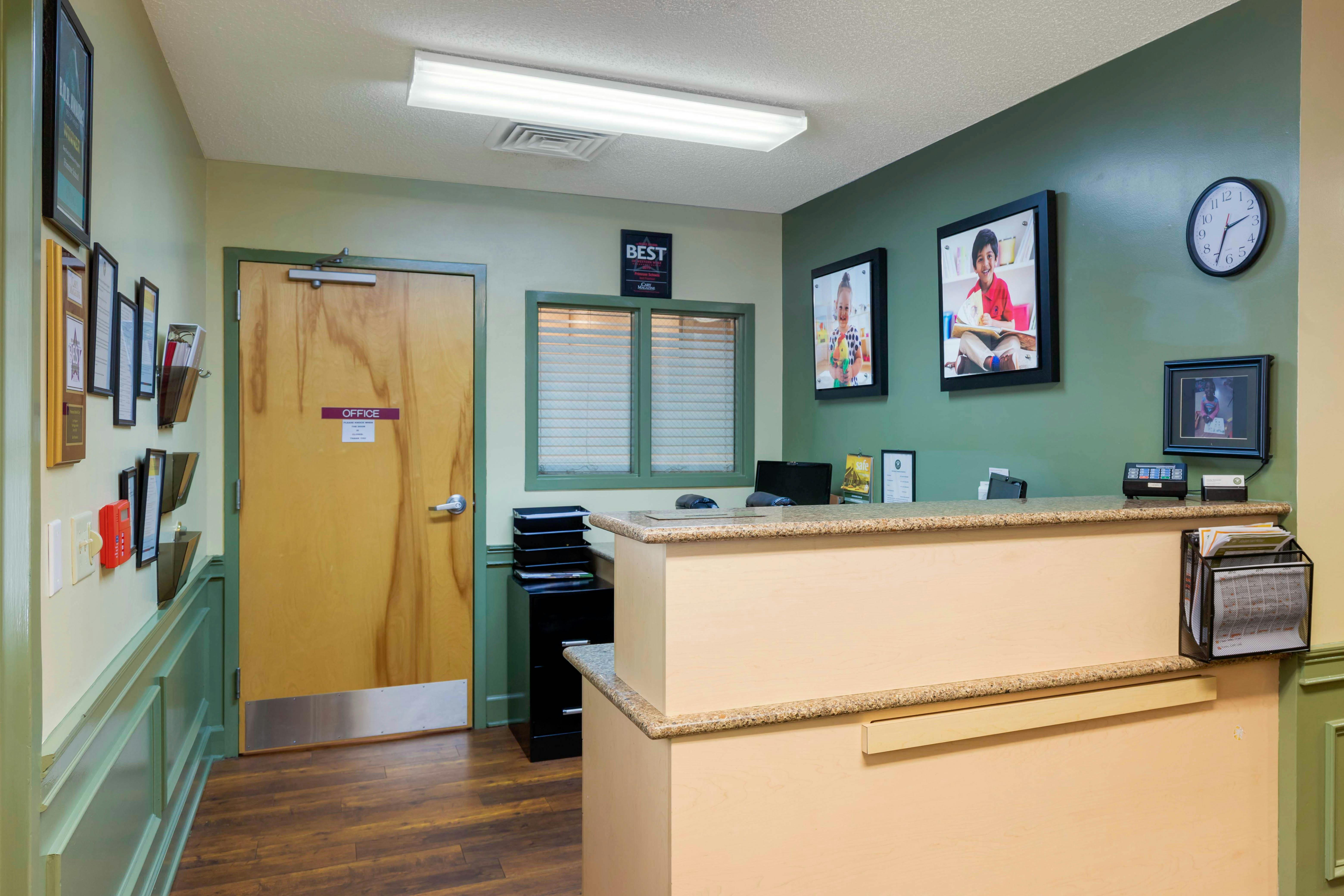 Reception desk with wood and green walls, framed children's photos, office door
