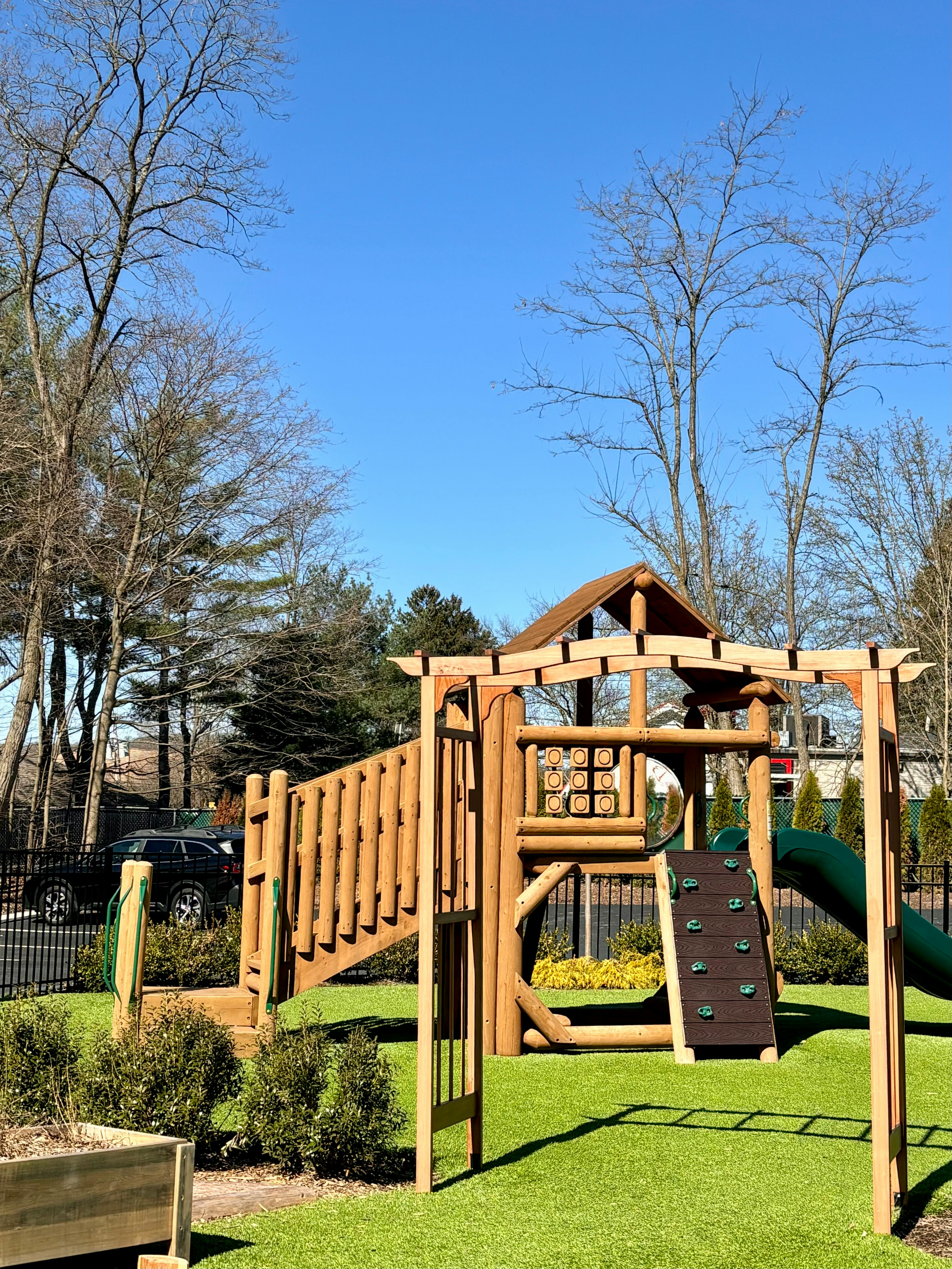 Wooden playground structure with a slide and climbing wall on green turf