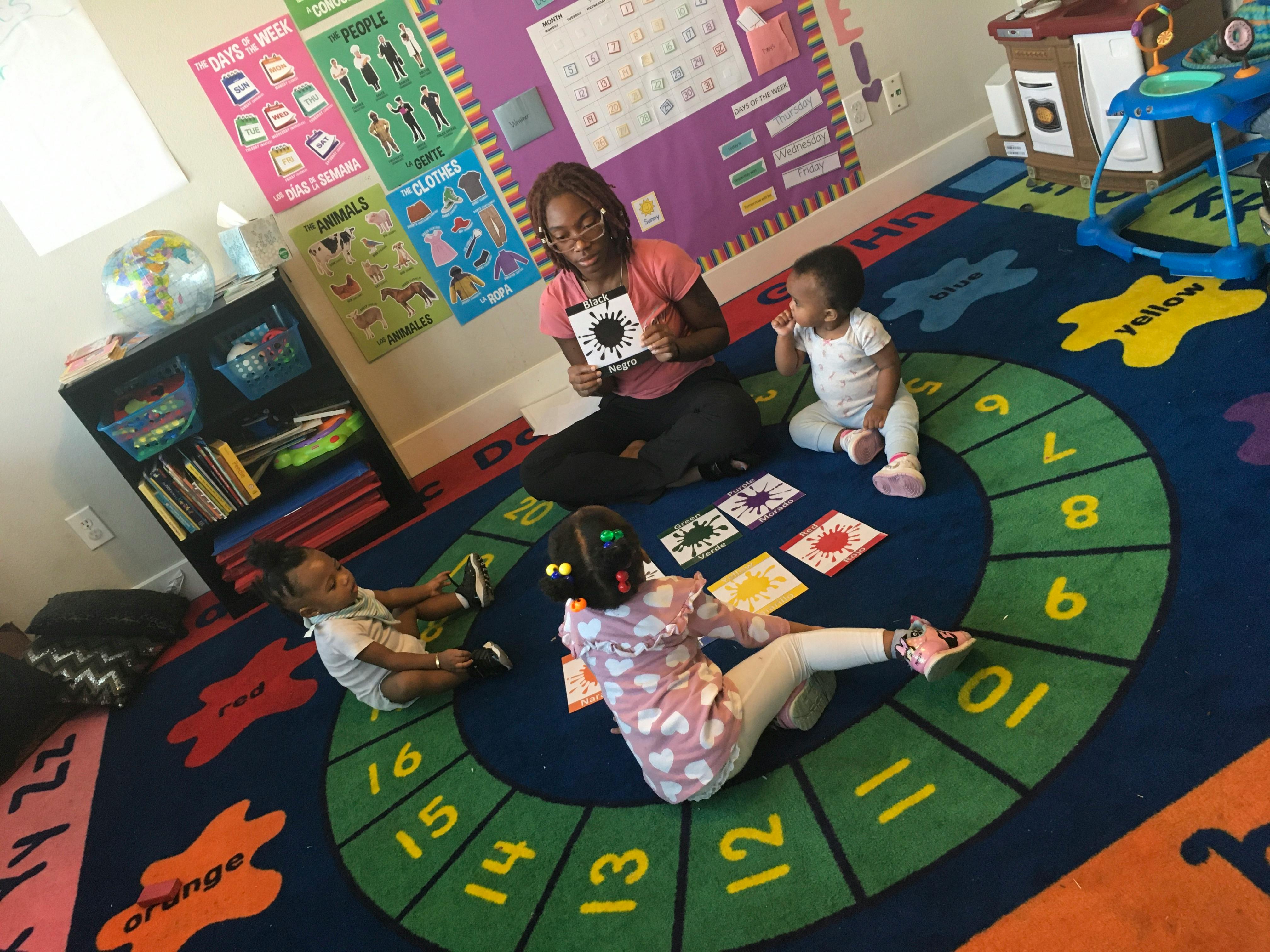 Person showing a card to three children on a number rug