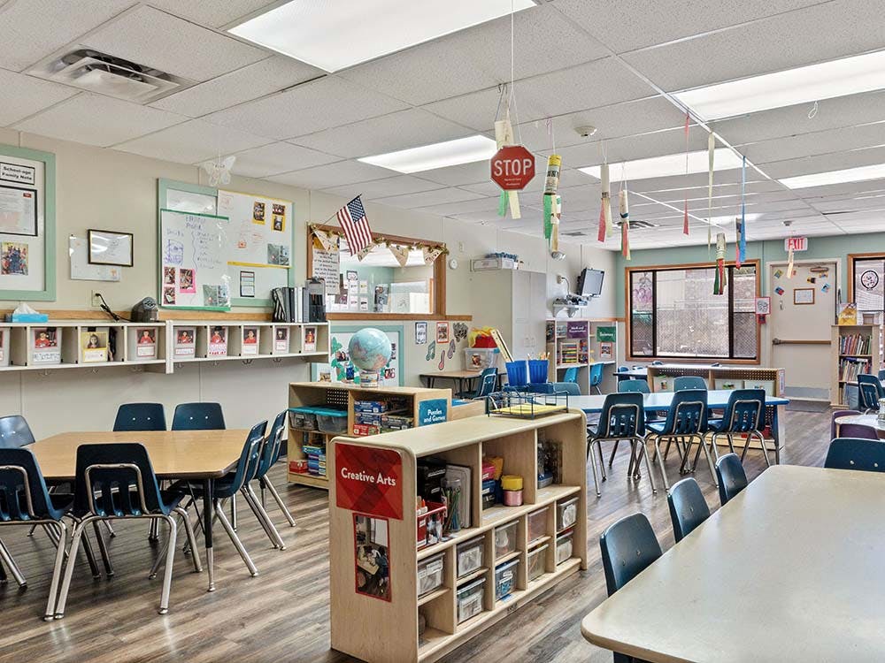Empty classroom with tables, chairs, and shelves of educational materials