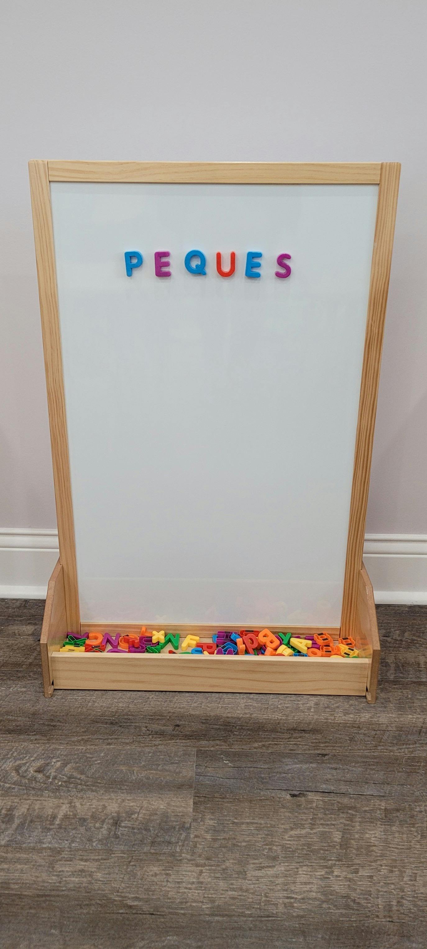 Whiteboard with colorful magnetic letters spelling "PEQUES" and more letters below