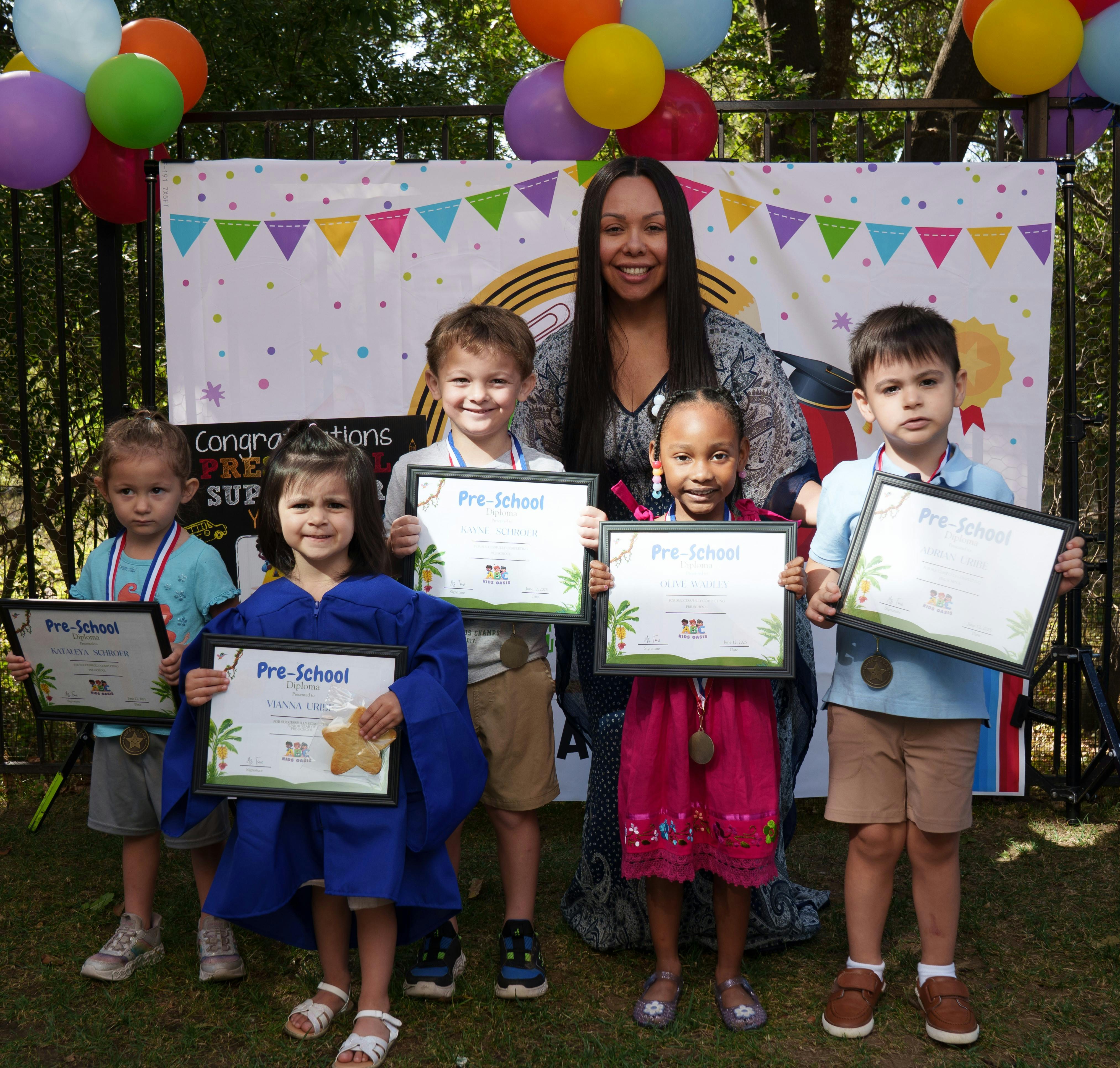 Adult and five children holding certificates that say "Pre-School"