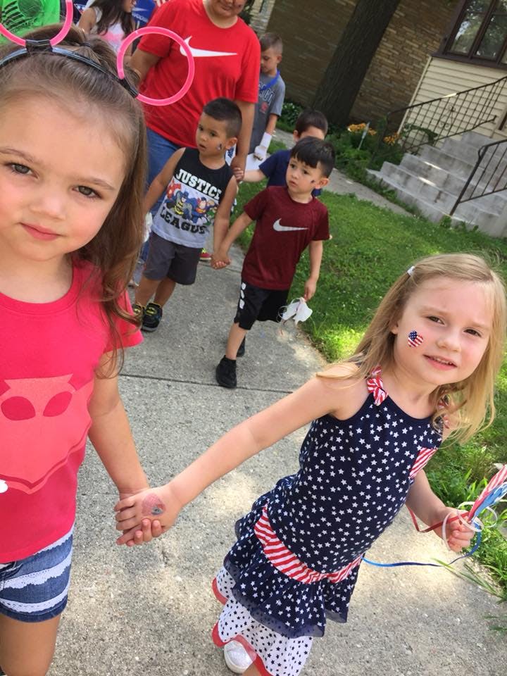 Two children holding hands, with other children and adults in the background