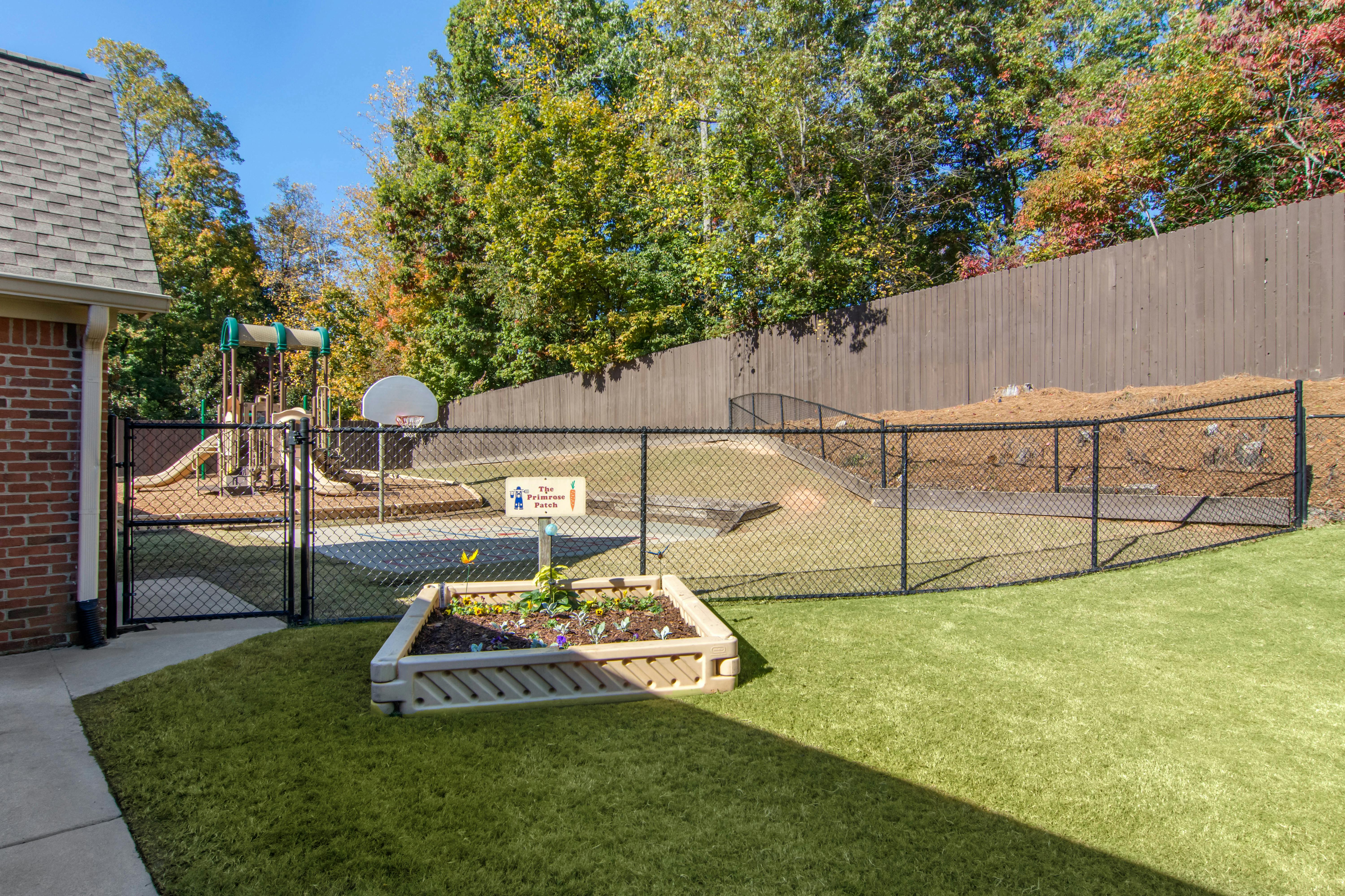 Playground behind a chain-link fence with a raised garden bed in the foreground
