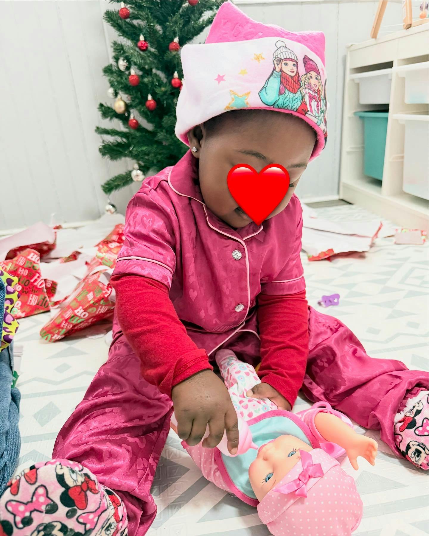Child in pajamas playing with a doll near a Christmas tree