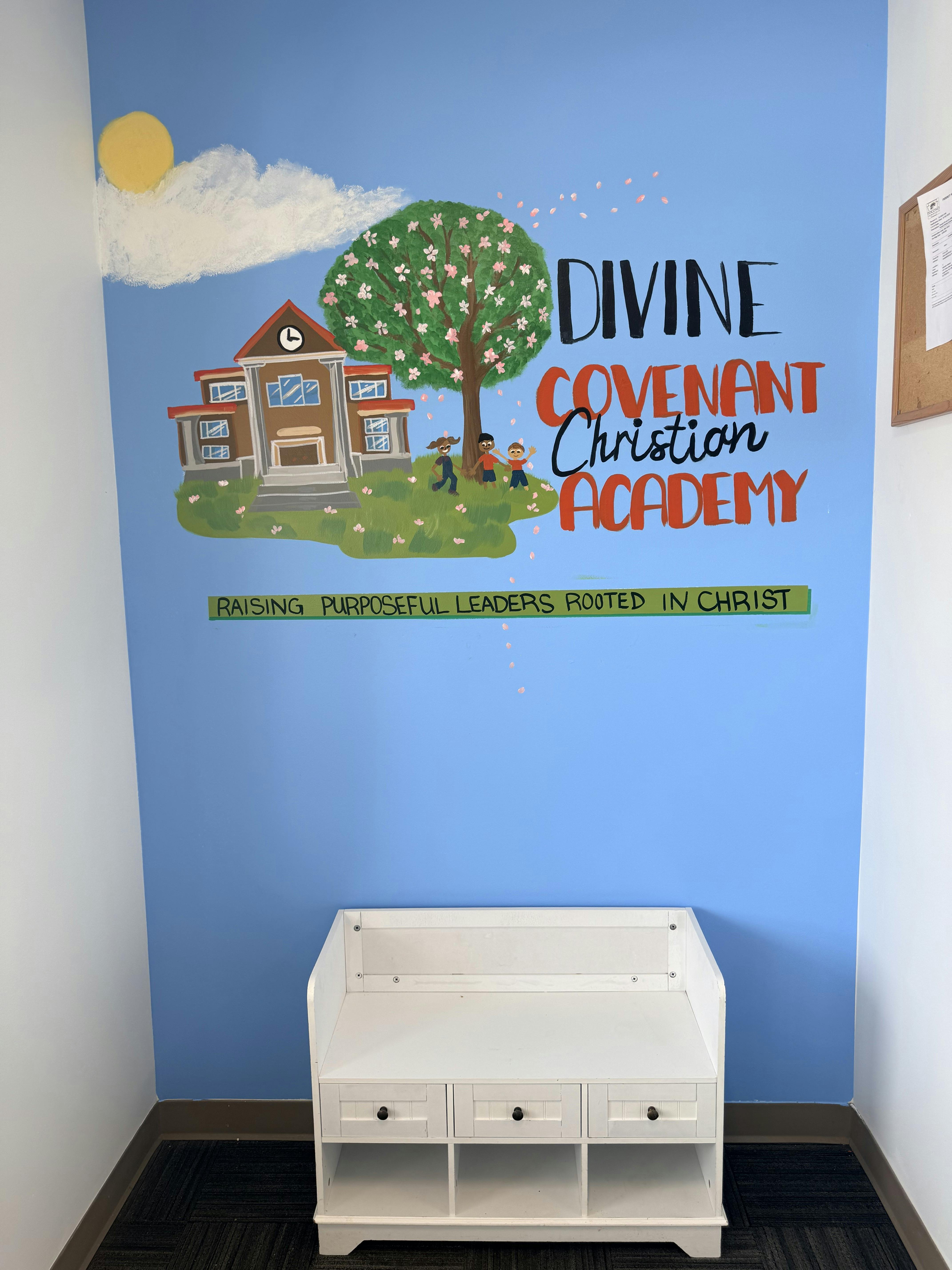 Mural of a school, tree, and children on a blue wall above a white bench