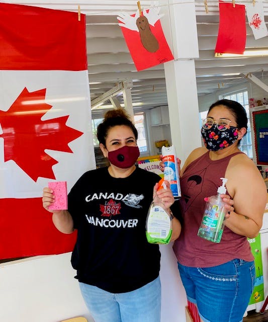 Two people in masks holding cleaning supplies in front of a Canadian flag
