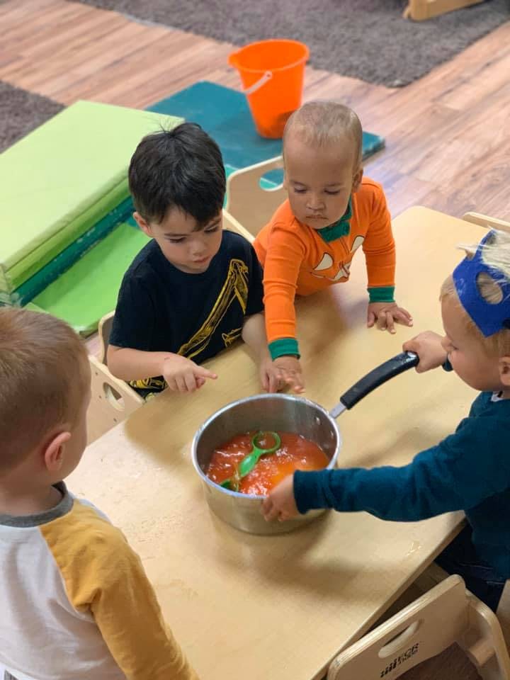 Children playing with a pot of orange liquid and a green spoon