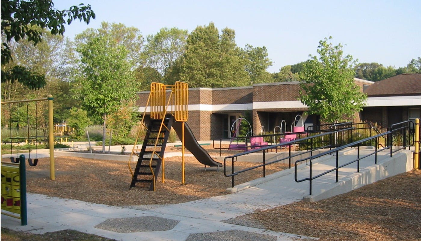 Playground with slide, swings, and accessible ramp leading to a building