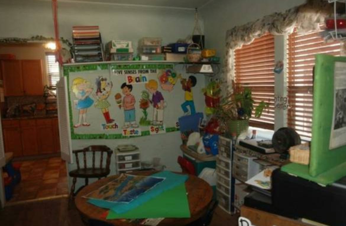 Room with a bulletin board displaying cartoon children and a table with papers