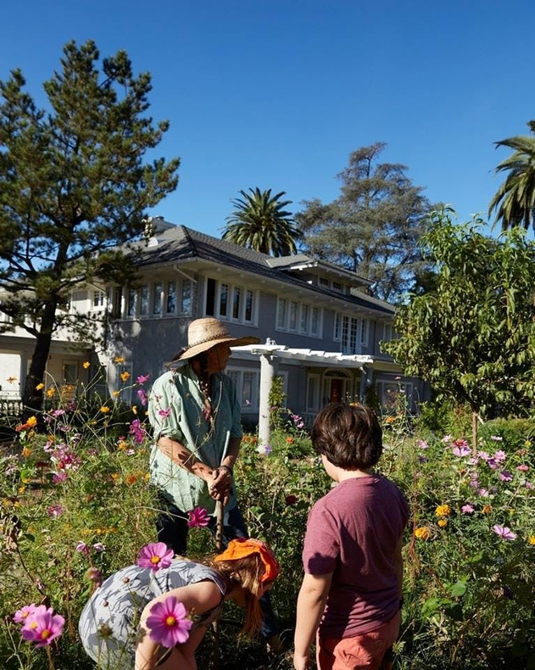 Adult and two children in a garden with flowers in front of a house