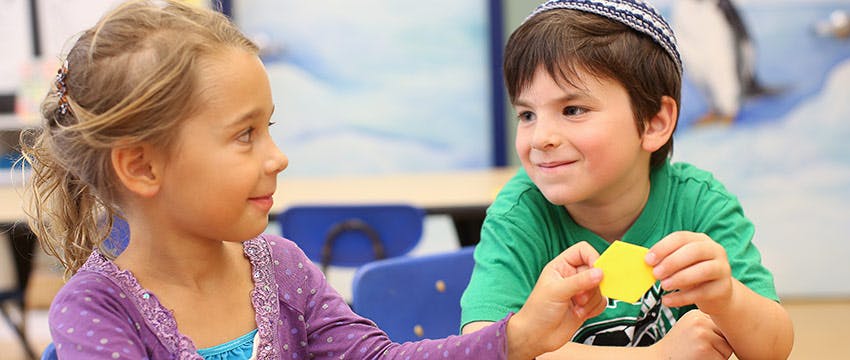 Two children interacting, one holding a yellow shape