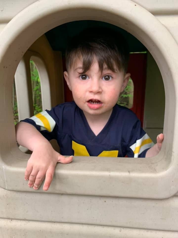 Child in a blue and yellow shirt looking out from a playhouse window