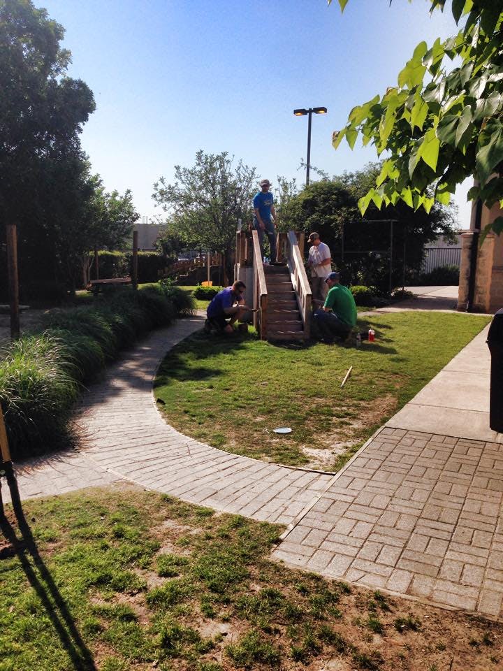 People working on a wooden play structure in a grassy area