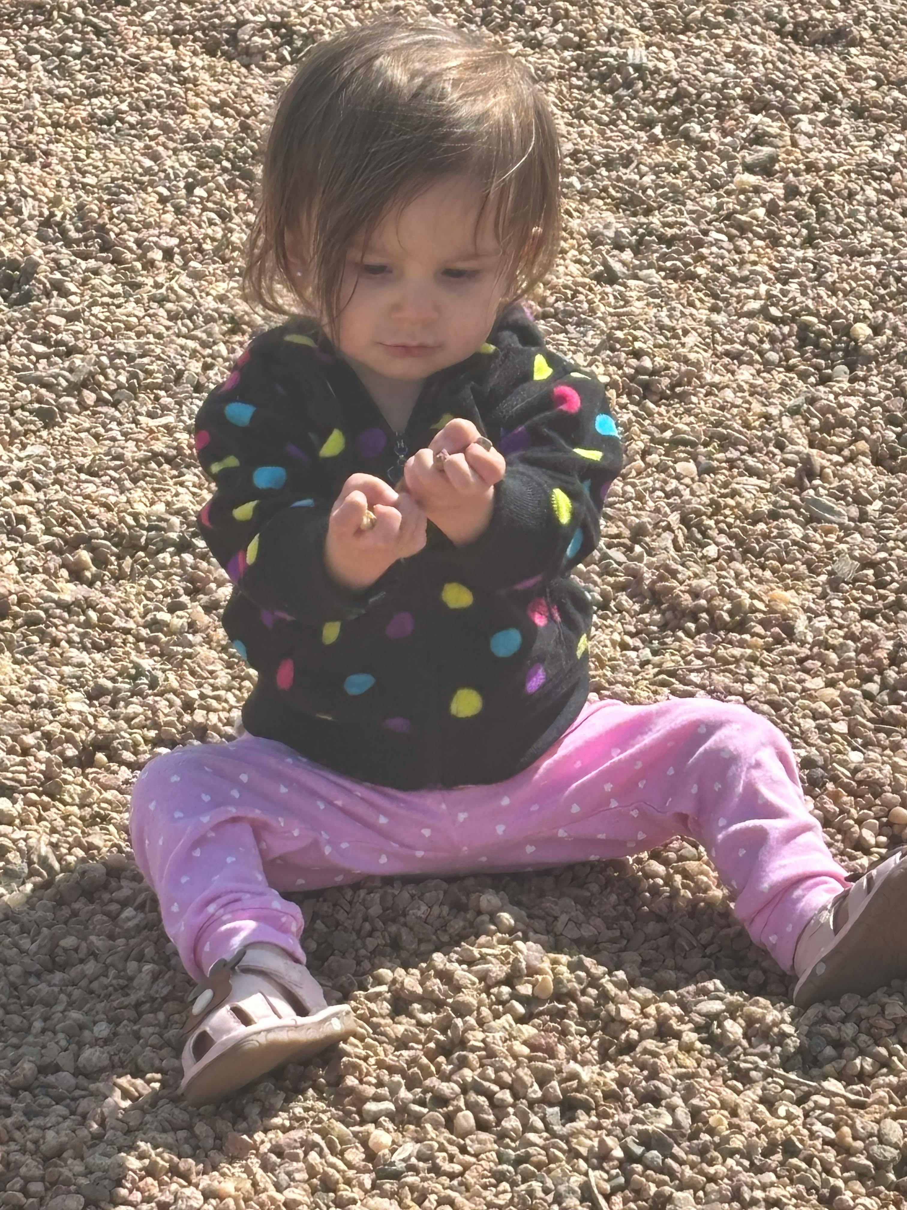 Child sitting on gravel, looking at hands