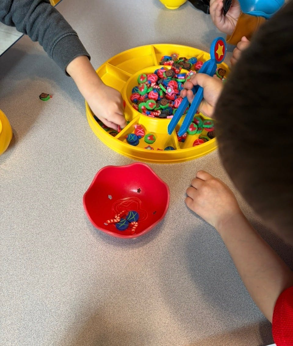 Children's hands sorting small colorful tokens from a yellow tray into a red bowl