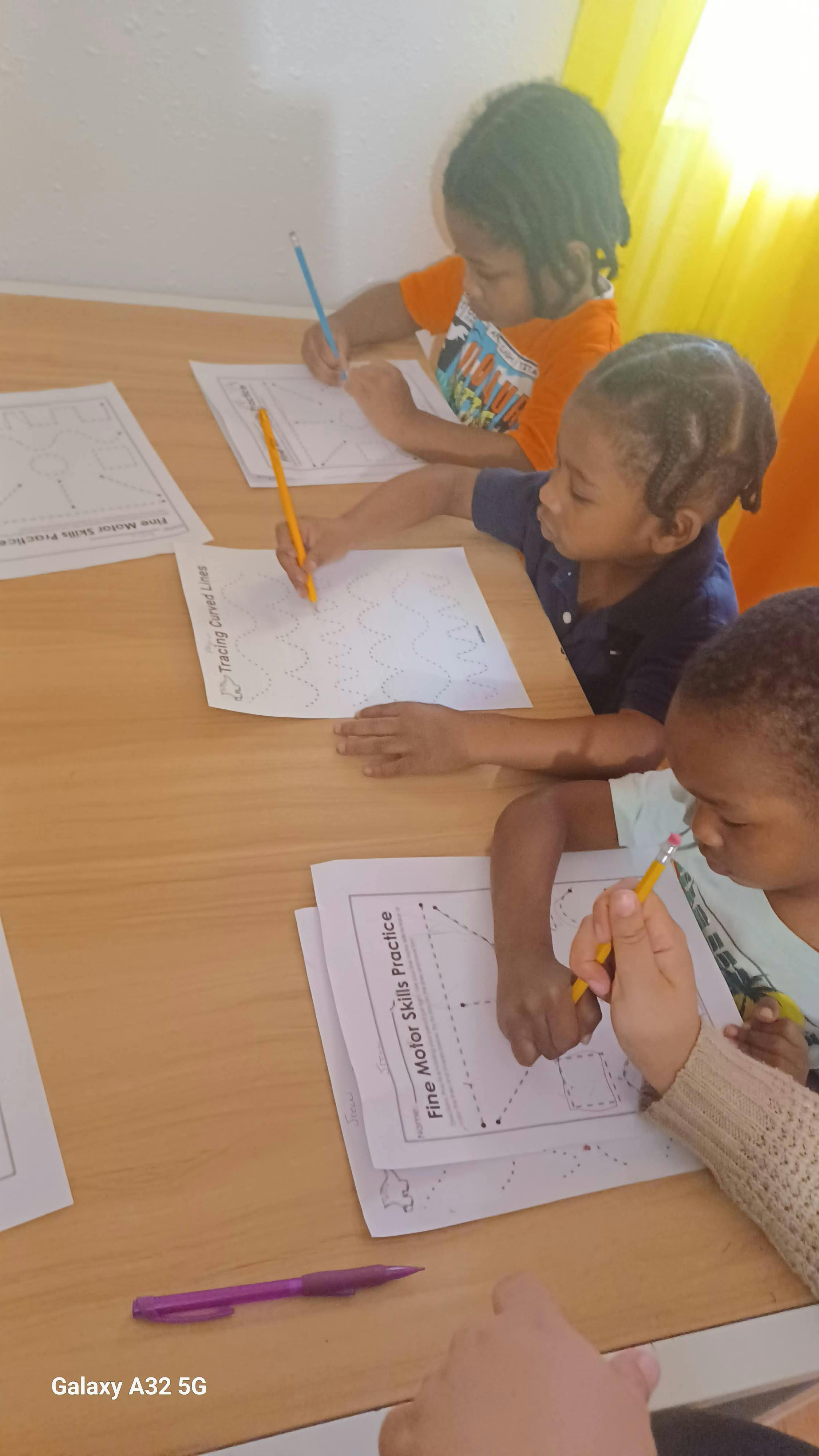 Three children practicing fine motor skills with tracing worksheets and pencils