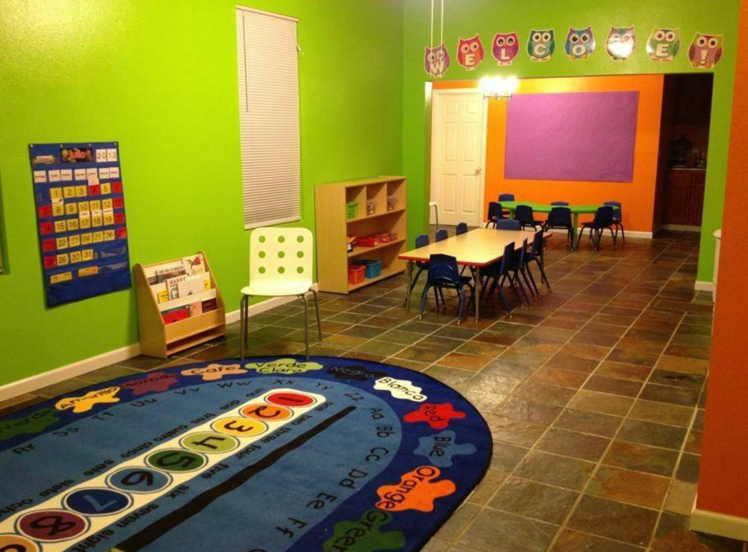 Classroom with a large rug, small tables and chairs, and green walls