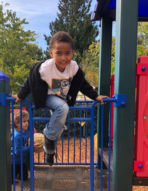 Child on playground equipment, another child with a basketball in the background
