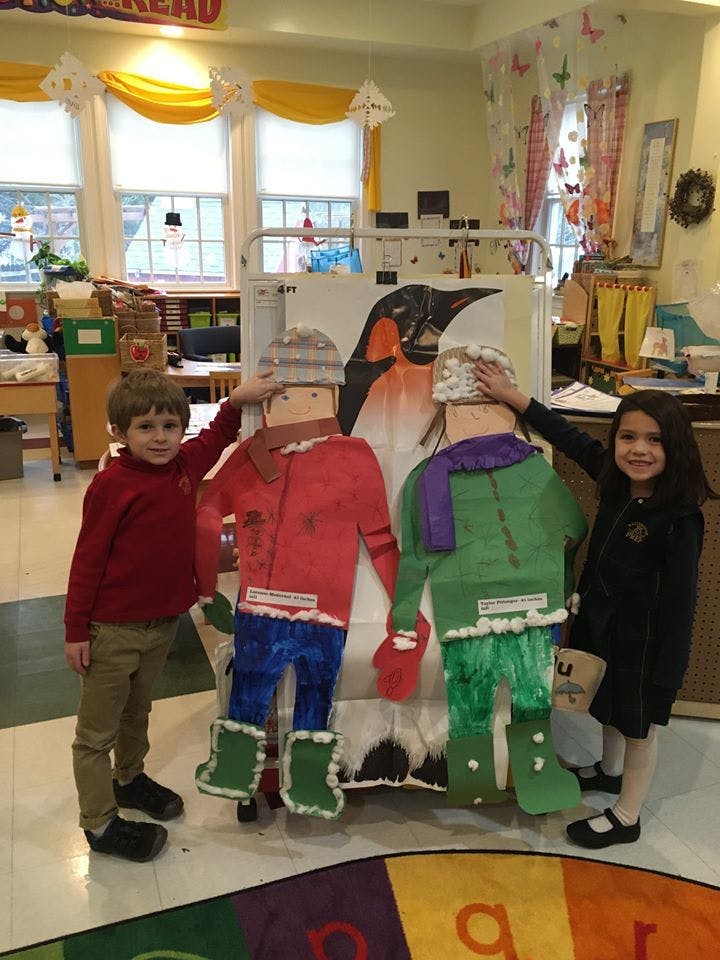 Two children standing next to paper cutouts of people in winter clothes