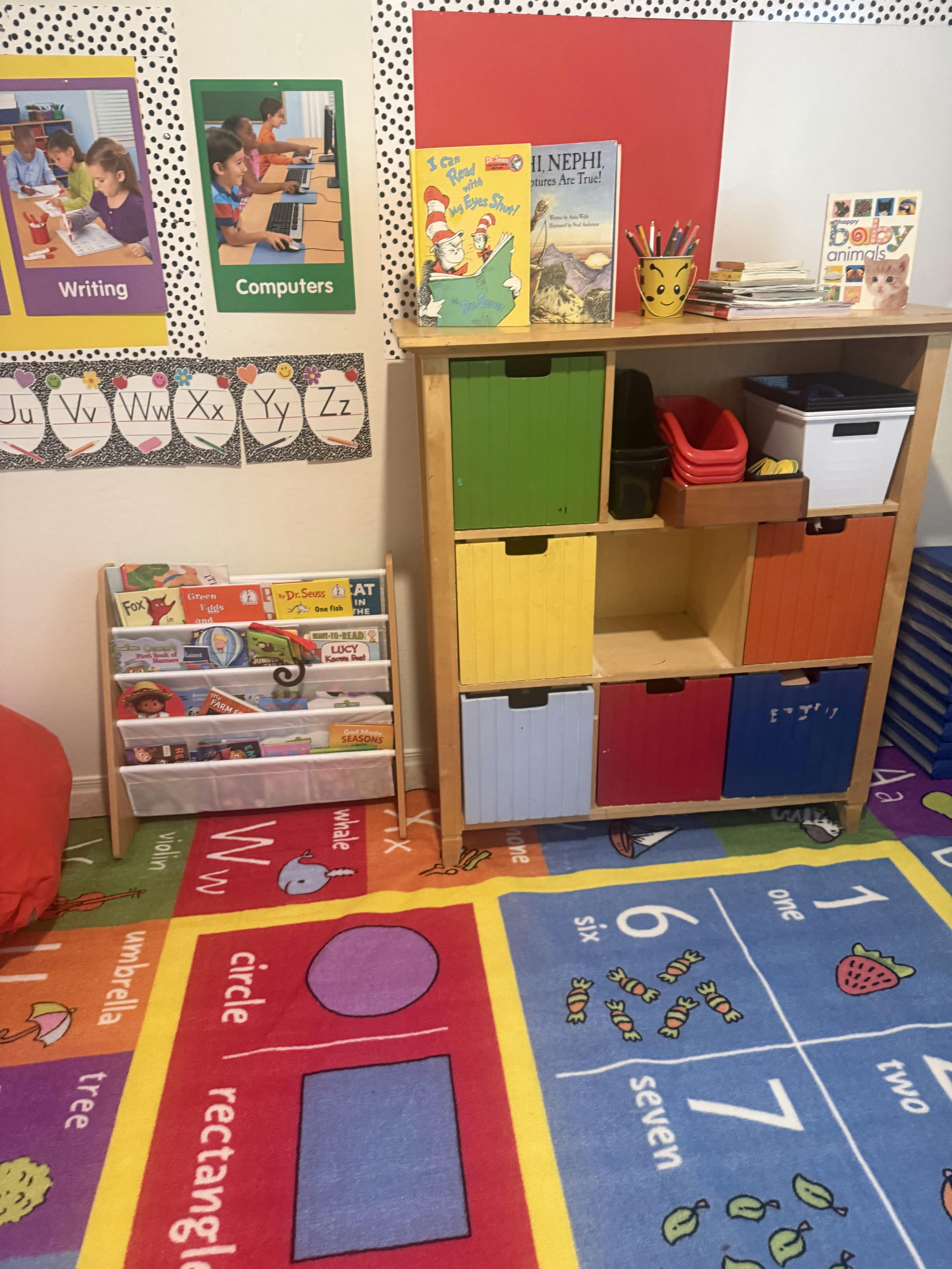 Classroom corner with an alphabet rug, book display, and shelves with colorful bins
