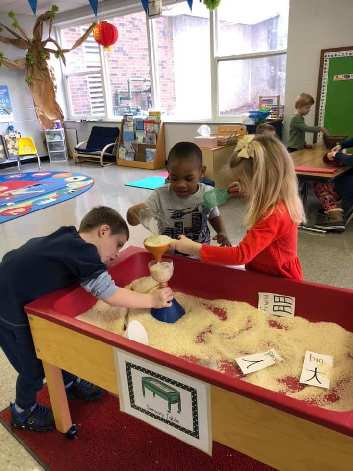 Three children playing with sand in a sand table
