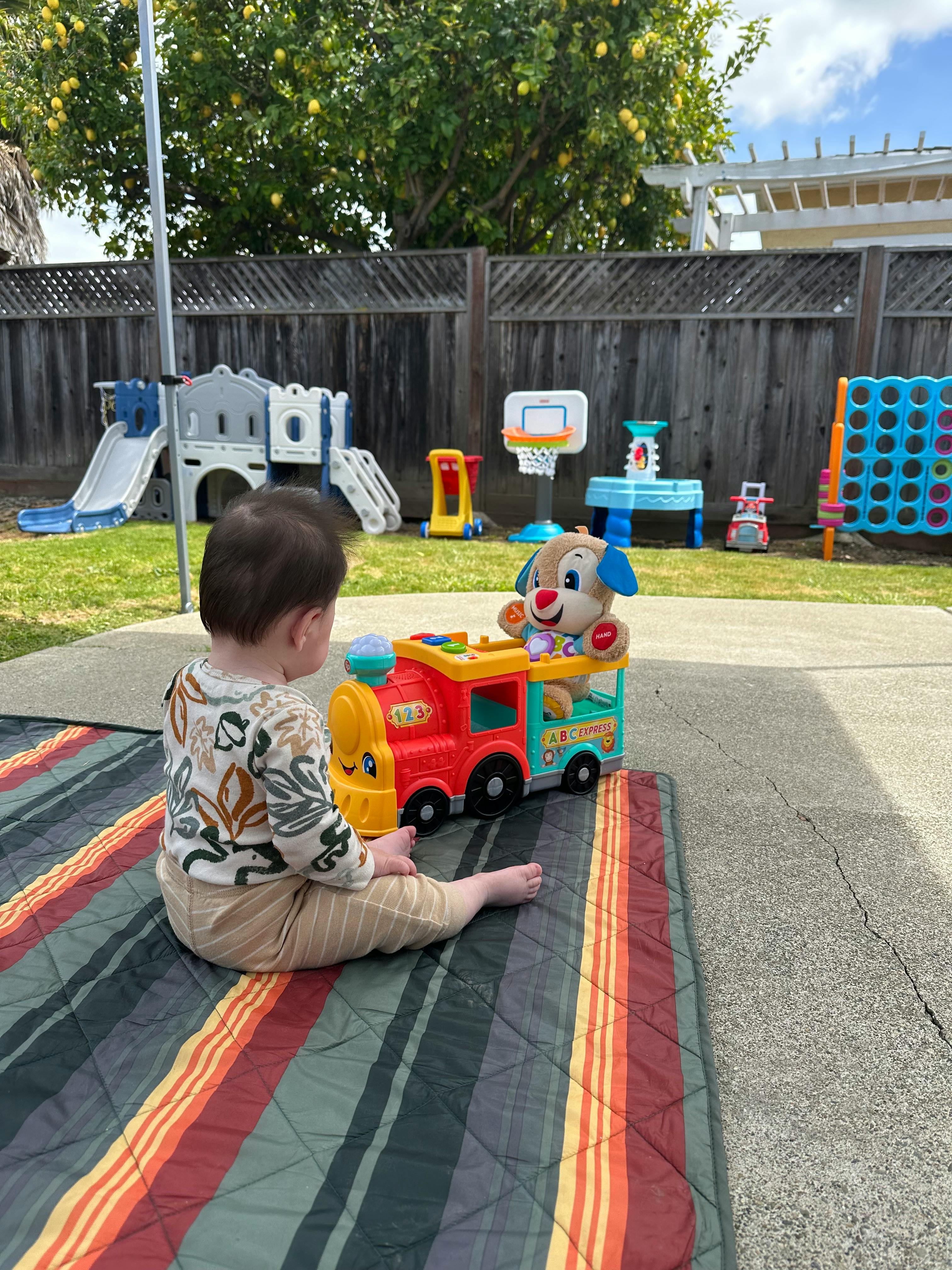 Child sitting on a striped blanket playing with a toy train