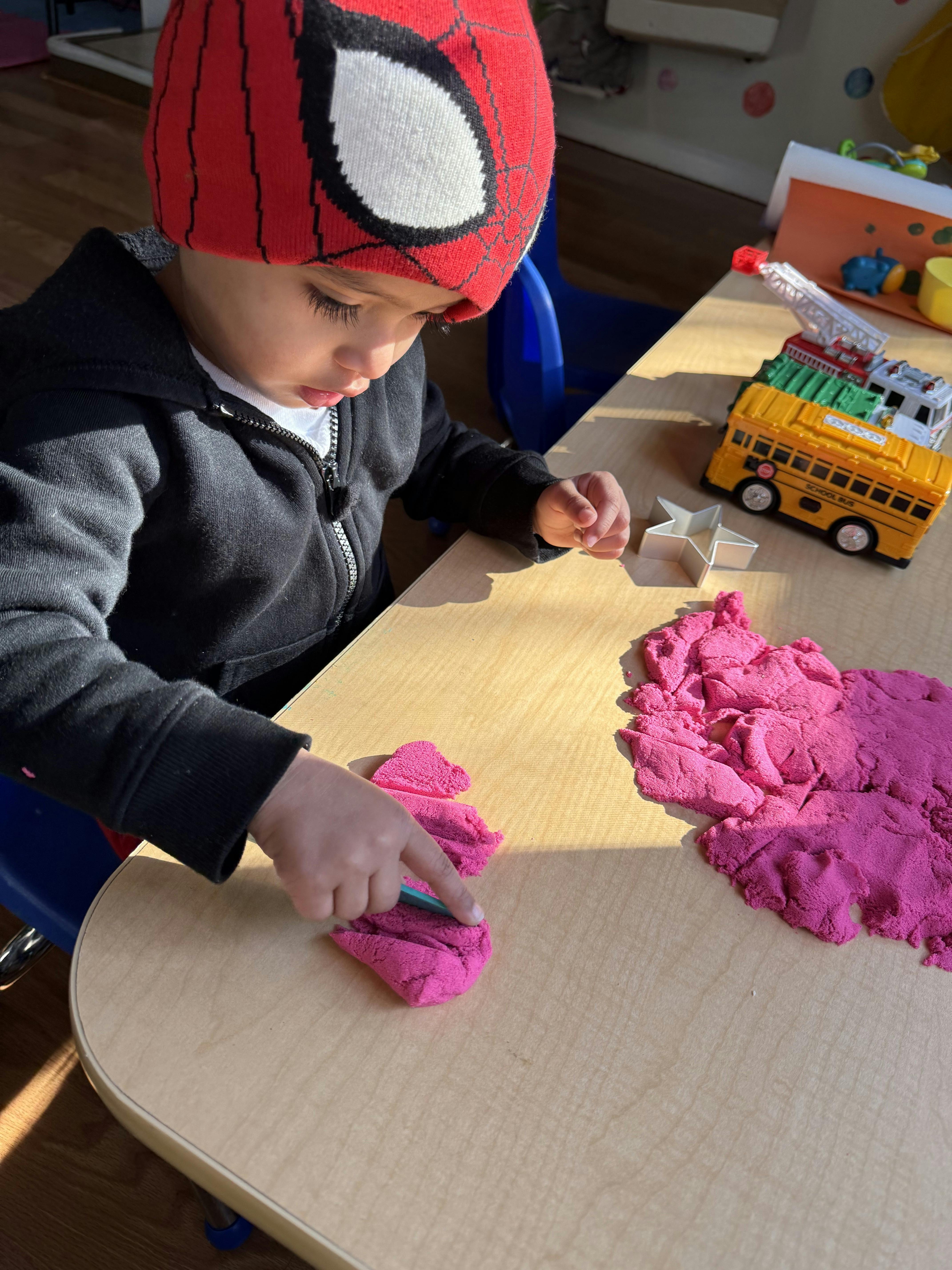 Child in a Spiderman hat playing with pink kinetic sand at a table